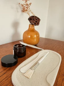 Spatules, pinceau à masque et pot ambré devant un vase ocre, La Divine Tourcoing