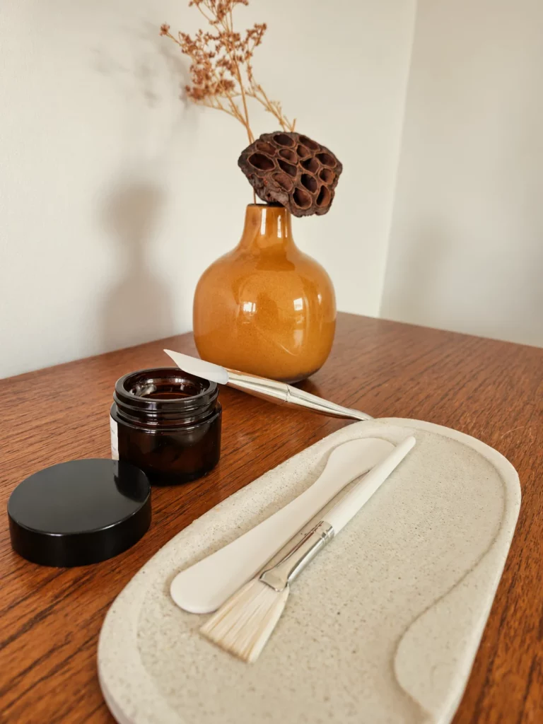 Spatules, pinceau à masque et pot ambré devant un vase ocre, La Divine Tourcoing