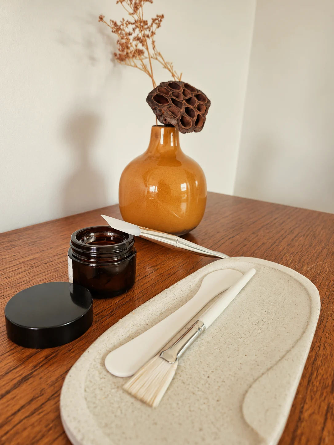 Spatules, pinceau à masque et pot ambré devant un vase ocre, La Divine Tourcoing
